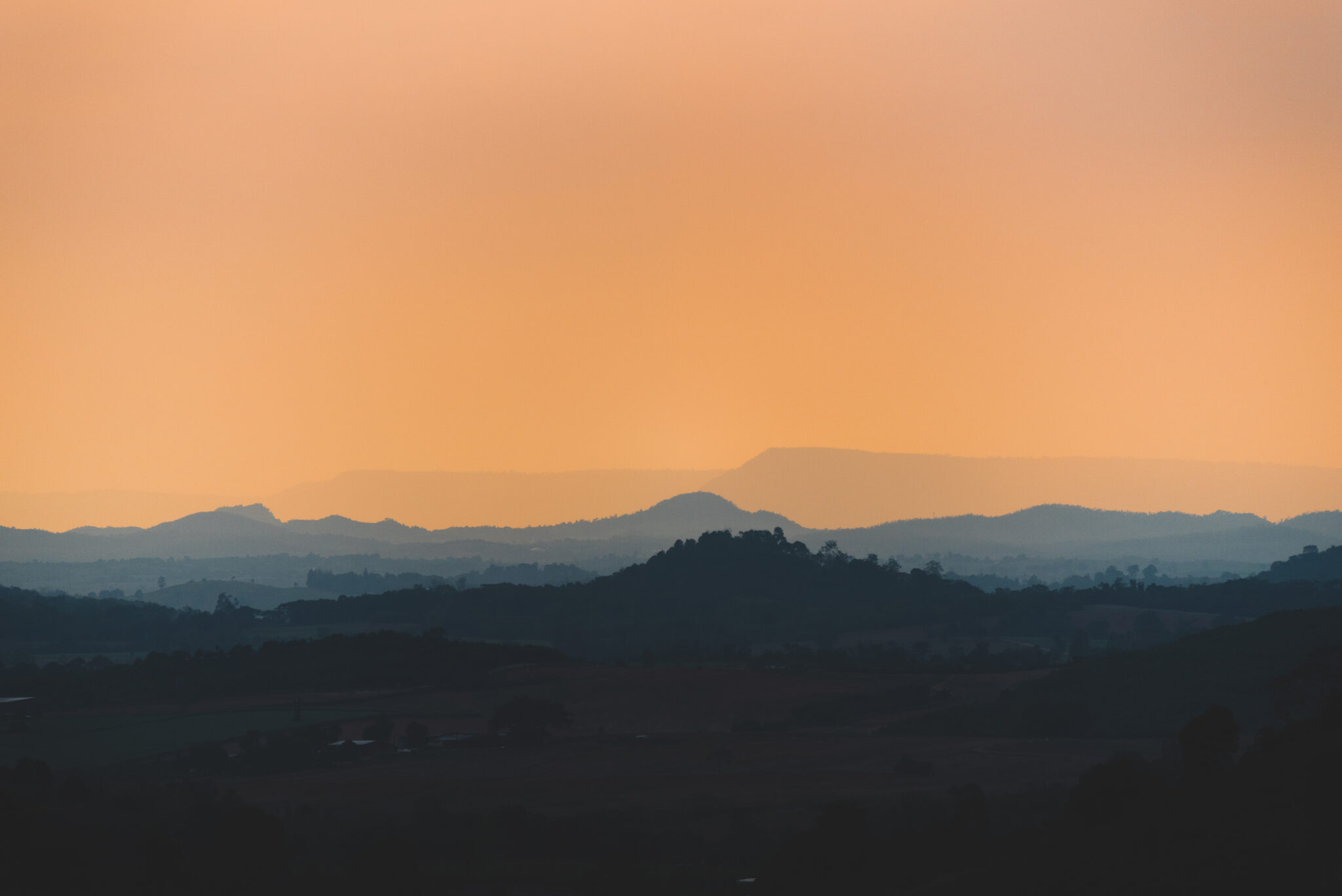 Nachfolgebegleitung: Blick auf orangefarbene Sonnenuntergangsstimmung über tropischen Bergsilhouetten, warmes Licht und weite Täler in ruhiger Dämmerung