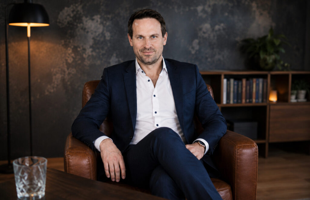 André Rehbein sitzt im dunklen Anzug entspannt in einem Ledersessel und blickt aufmerksam in die Kamera eines Büros.